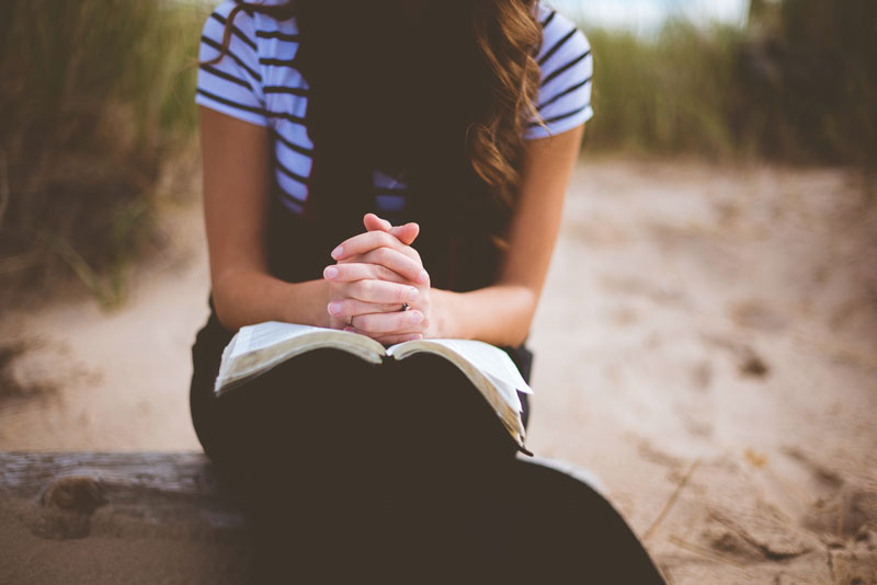 Woman seated with hands folded on top of an open Bible